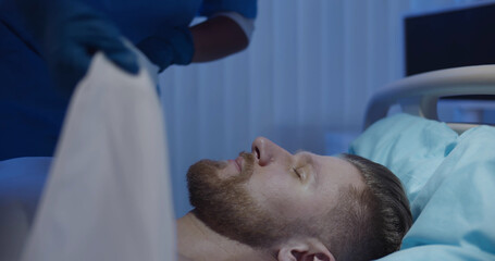 Close up of medical worker on gloves covering dead male patient with sheet