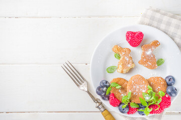 Funny bunny pancakes, Cute Kids Breakfast for Easter morning. Creative rabbits pancakes with fresh berry decoration, top view on white wooden background copy space