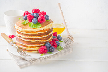 Stack of classic  American pancakes with fresh berries and maple syrup, on white table background copy space