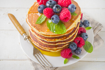 Stack of classic  American pancakes with fresh berries and maple syrup, on white table background copy space