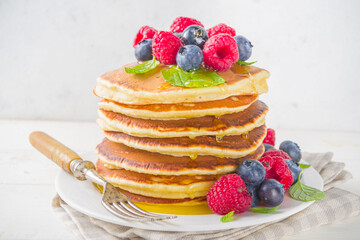Stack of classic  American pancakes with fresh berries and maple syrup, on white table background copy space