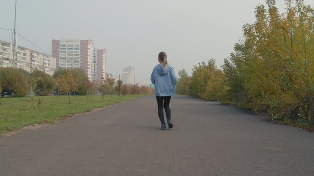Tilt up slowmo of young woman in hoodie running in city on foggy autumn morning