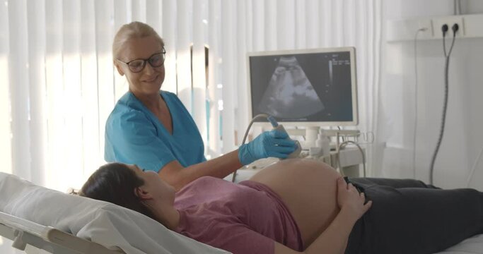 Senior doctor doing ultrasound scan for young pregnant woman in hospital.