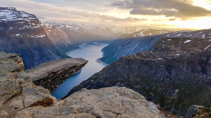 Famous rock formation, Trolltunga with a view from the above on Ringedalsvatnet lake, Norway. Rock hanging. Slopes of the mountains are partially covered with snow. Soft colors of the sunrise