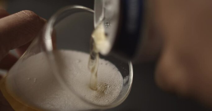 4K Slow motion Asian man hand (blur, out of focus) holding a beer can and pouring beer into a clear glass, time to relax on vacation ,White beer bubble, blackmagic 4k shot, beverage concept.