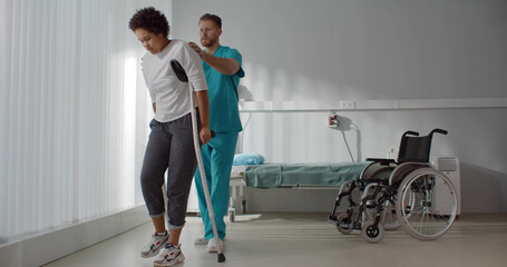 Male medical nurse assisting african young woman walking with crutches
