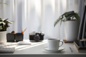 White coffee cup on and mouse keyboard with camera and plant pot on white wooden table