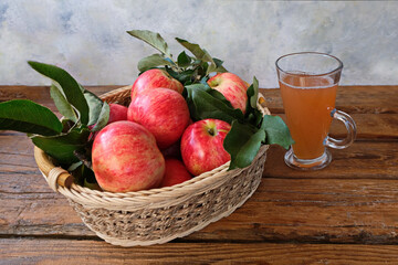 Pink striped apples with leaves in a wicker dish on a brown wooden table.  Next to it is a glass of freshly squeezed juice. Диетические фрукты, здоровое питание.
