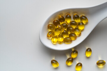 A white spoon filled with yellow vitamin D3 capsules on a white table. As concept of support ...