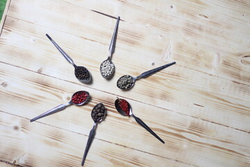 Various peppers: white, green, black, red, pink, allspice in vintage spoons on wooden table