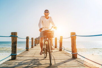 Portrait of a happy smiling man dressed in light summer clothes and sunglasses riding a bicycle on...