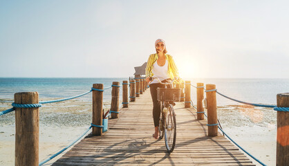 Portrait of a happy smiling woman dressed in light summer clothes and sunglasses riding a bicycle...