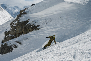 A male snowboarder rides a snowboard in the mountains on fresh snow. Freeride in the mountains.