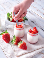hand with teaspoon on a natural yogurt with fresh strawberries