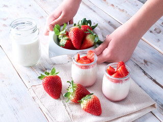 hands holding a bowl with fresh strawberries, yogurt and glass of milk