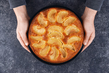 Man holding baked apple pie in hands on black background