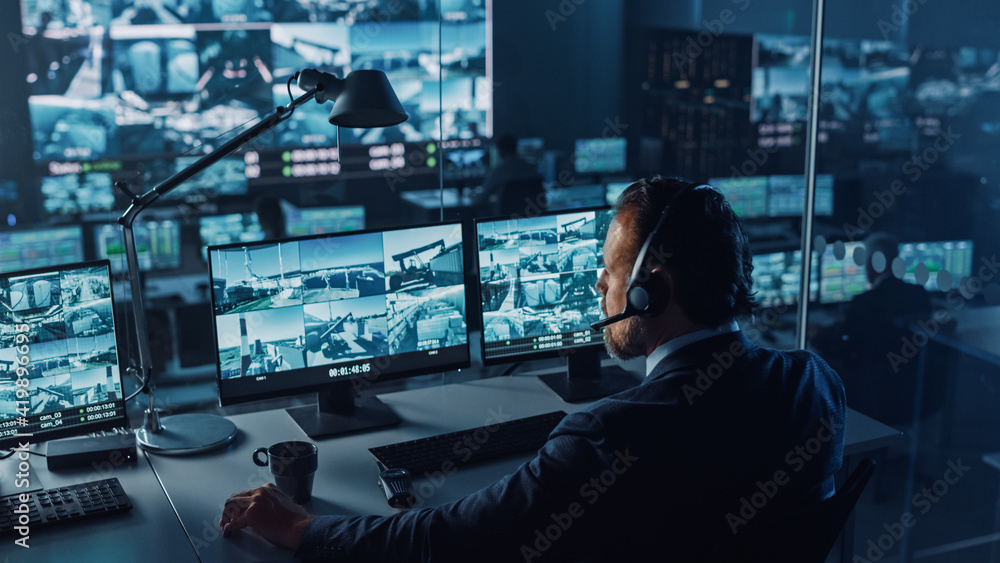 Aufkleber Male Officer Works on a Computer with Surveillance CCTV Video in a Harbour Monitoring Center with Multiple Cameras on a Big Digital Screen. Employees Sit in Front of Displays with Big Data.