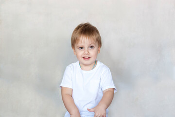 Fototapeta premium Portrait of a cute little boy in a white t-shirt. Children's emotions. Child on the background of the wall. Success, bright idea, creative ideas and concepts.