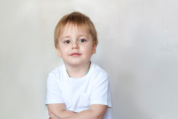 Fototapeta premium Portrait of a cute little boy in a white t-shirt. Children's emotions. Child on the background of the wall. Success, bright idea, creative ideas and concepts.