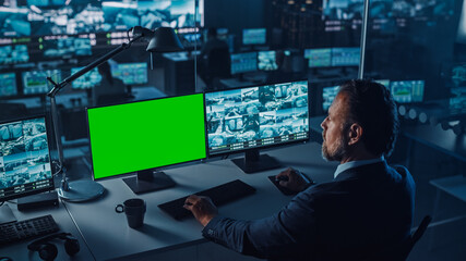 Male Officer Works on a Computer with Surveillance CCTV Video and Green Mock-up Chroma Key in a...