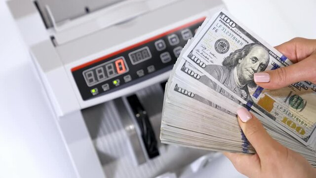 Bundle of one hundred dollar banknotes. Female's hands holding a large sum of money of dollar bills on the background of automatic counting machine.