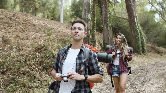 Couple of hikers with film camera taking photos of landscape while walking on forest path, enjoying outdoor vacation and healthy recreation. Adventure travel concept