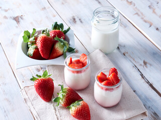 wooden table with a couple of natural yogurts and fresh strawberries and a glass of milk