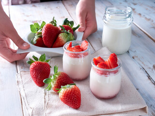 hands holding a bowl with strawberries, natural yogurt and glass of milk also on display