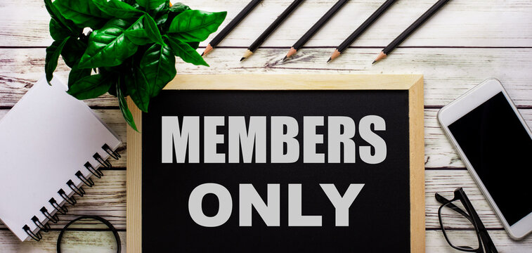 MEMBERS ONLY Is Written In White On A Black Board Next To A Phone, Notepad, Glasses, Pencils And A Green Plant.