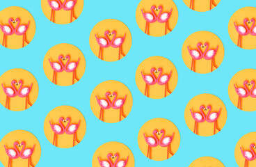 Pattern created of two flamingo toys in orange circle on neon blue background. Top view.