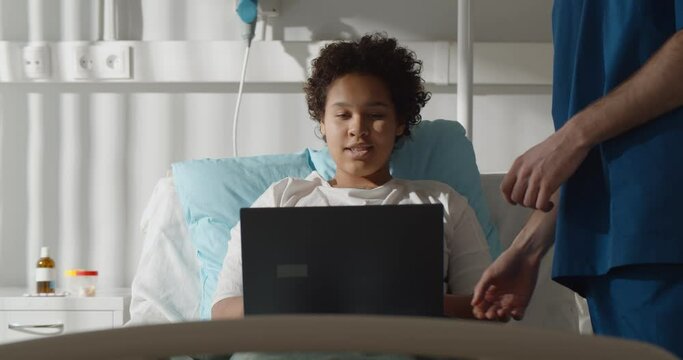 Doctor taking laptop from african female patient resting in hospital ward