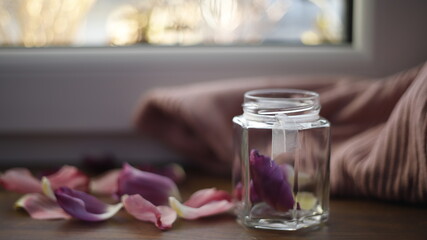 Słoik szklany przezroczysty z płatkami tulipanów fioletowymi na parapecie przy oknie w dzień  - obrazy, fototapety, plakaty