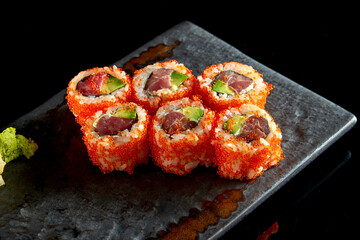 California sushi roll with tuna, avocado, cucumber and tobiko caviar served on a plate with wasabi and ginger. Isolation on a black background. Japanese food