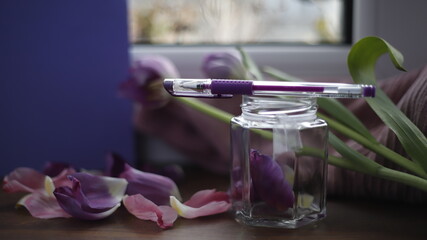 Słoik szklany przezroczysty z płatkami tulipanów fioletowymi na parapecie przy oknie w dzień  - obrazy, fototapety, plakaty