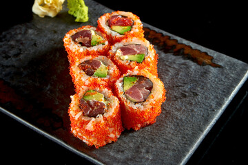 California sushi roll with tuna, avocado, cucumber and tobiko caviar served on a plate with wasabi and ginger. Isolation on a black background. Japanese food