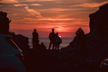 Group of people silhouette admiring a beautiful red and orange sunset in a famous sunset point in...