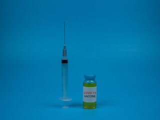 An image of a vial covid-19 vaccine and syringe isolated on a blue background. Healthcare and medical concept. Selective focus image.