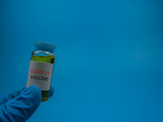 An image of person holding vial covid-19 vaccine isolated on a blue background. Healthcare and medical concept. Selective focus image.