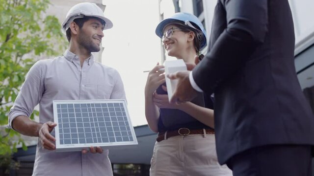 Group of businessmen and meeting engineers to install solar panels in building. Consulting team for building an eco-friendly building structure. Exchange of ideas on work of construction team.