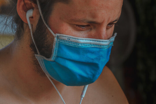 Close up of a man wearing headphones and a medical mask showing concept of daily life during the new normal or covid-19 pandemic