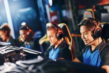 Playing to win. Happy asian male cybersport gamer wearing headphones participating in eSport...