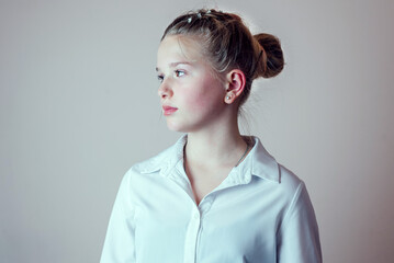 Side view portrait of young blonde girl with her hair put in a bun wearing white shirt