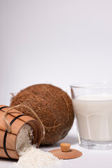 fresh coconut near wooden bowl with coconut flakes and glass of coco milk. isolated on white background. tropical nut