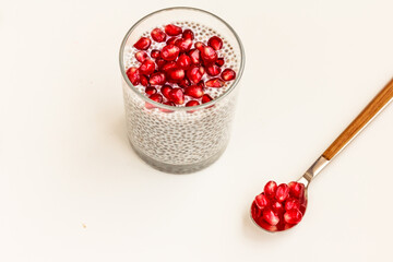 Quick and healthy meal concept . Chia seed Pudding and red pomegranate seeds in a glass, spoon on white background.. Stock photo, top view, copy space
