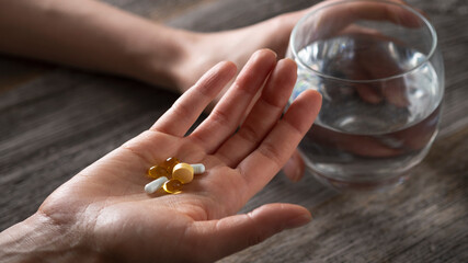 Women hands holding pills diffrent shape and colors and glass of water. Supplements or antibiotic