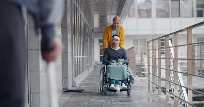 Female nurse pushing a disabled man in wheelchair outside hospital