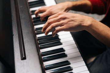 Obraz premium Close-up hands of unrecognizable man playing on piano at home recording studio. Closeup side view fingers of male playing digital electronic piano synthesize. Concept of music education.