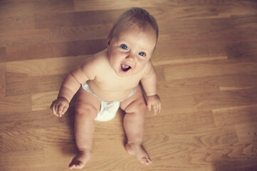 Little cute baby sitting on the floor and smiling in diaper