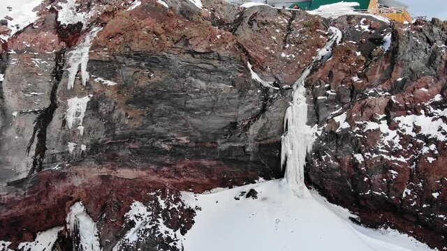 Wonderful steep bare cliff with frozen waterfalls and ski resort station with moving poma lift on sunny winter day aerial view