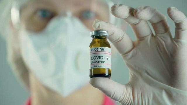 Close up medical researcher in face protective mask holding ampoule or bottle with anti coronavirus moderna vaccine in bacteriological laboratory